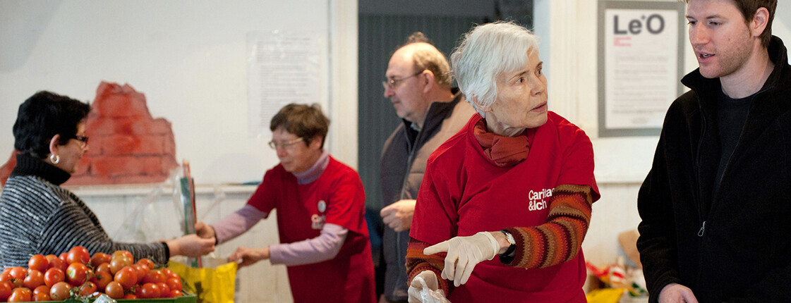 Freiwillige des Caritas-Projekts LE+O verteilen Lebensmittel und beraten Besucherinnen und Besucher in einer Ausgabestelle.