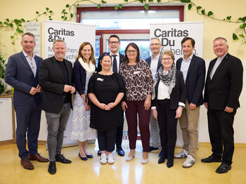 Mitarbeiter*innen der Caritas posieren in einem Raum vor einem Banner der Caritas. 