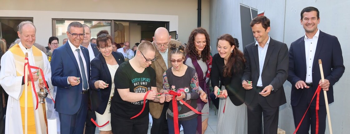 Viele Menschen durchschneiden mit ihren Scheren das rote Band zur Feierlichkeit der Eröffnung des Wohnhaus' Laa.