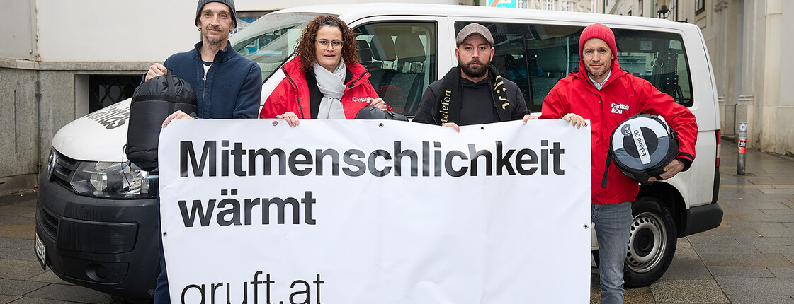 Ein Ex-Klient, Judith Hartweger, Christopher Seiler und Klaus Schwertner halten Schlafsäcke und ein Transparent mit der Aufschrift Mitmenschlichkeit wärmt